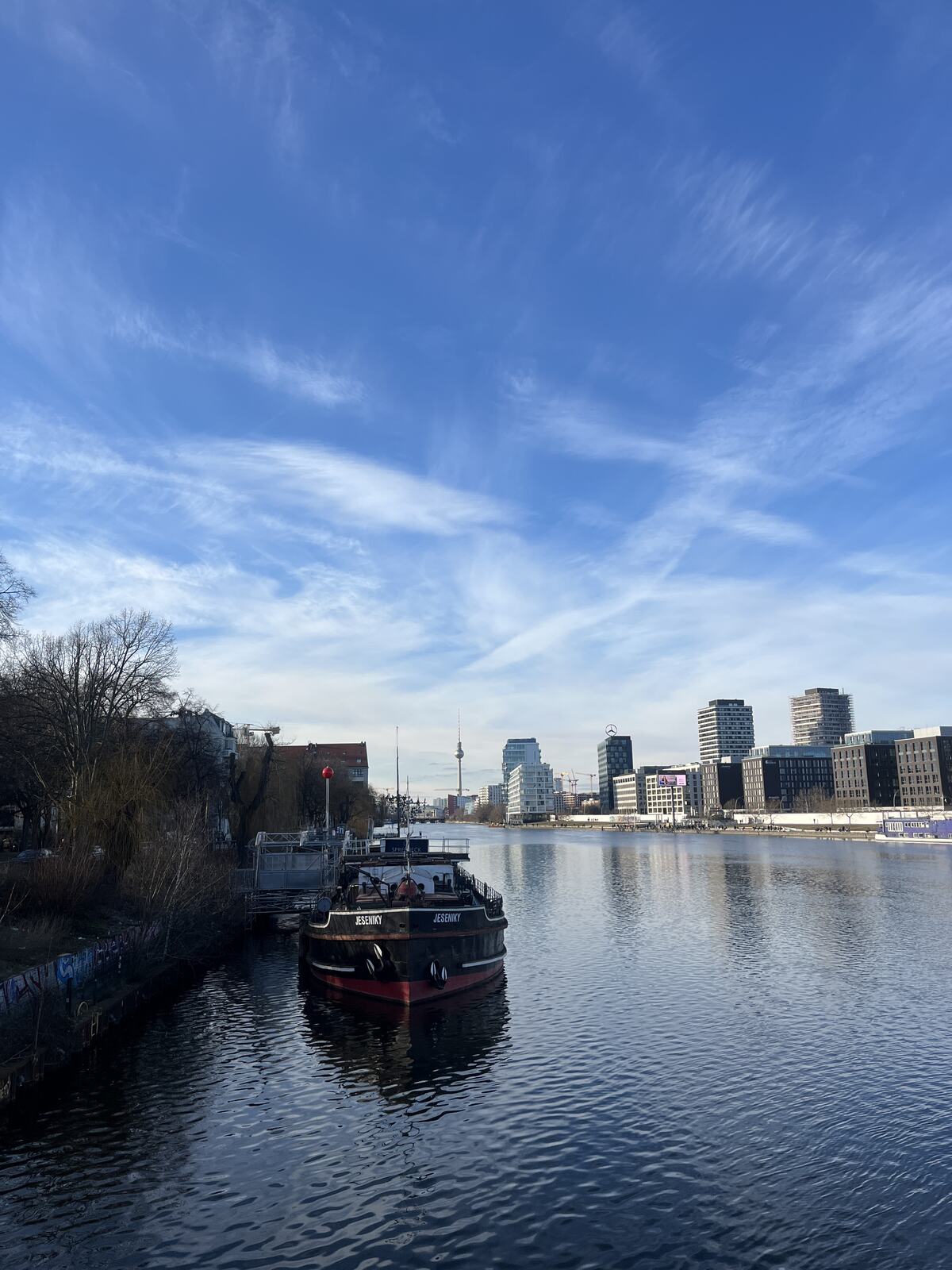 A boat moored on the Spree river with the Berlin skyline behind it
