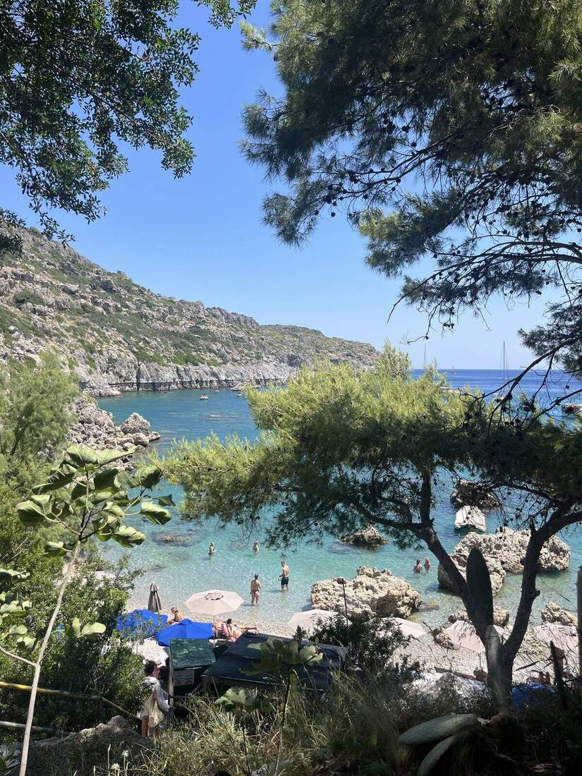 A turquoise cove with swimmers, beach umbrellas, and limestone cliffs in Rhodes