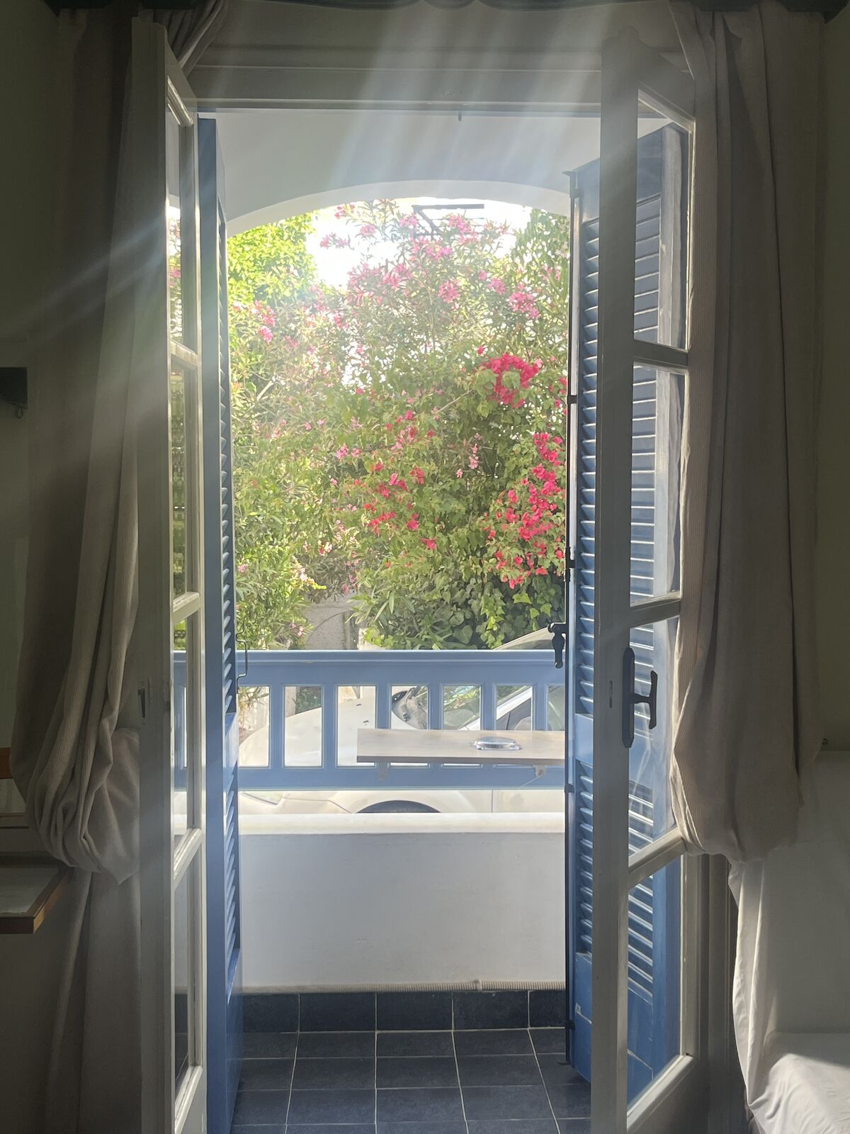 An open shuttered window framed by bougainvillea in Greece