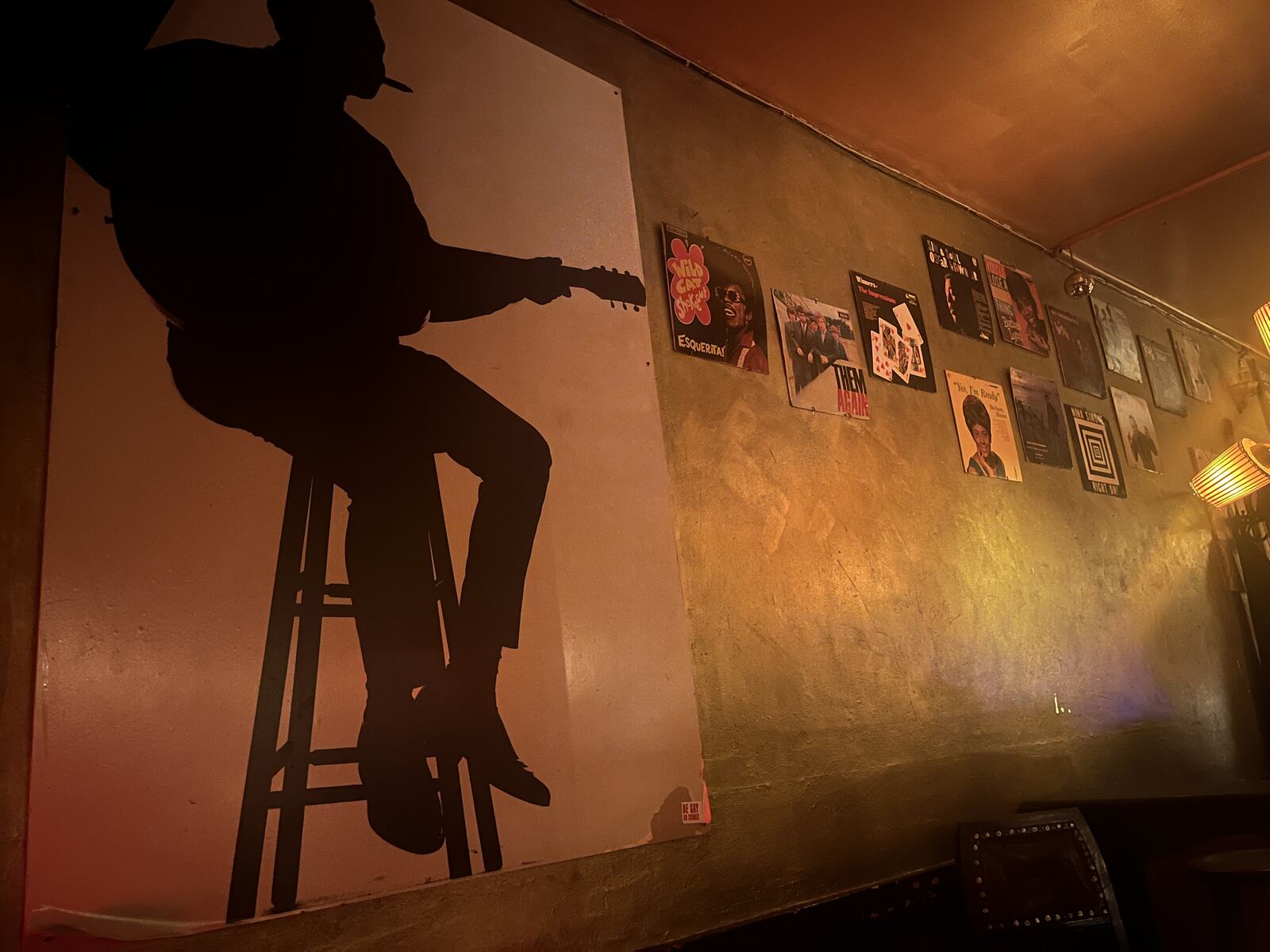 A silhouette of a musician on a stool beside a wall of vinyl records