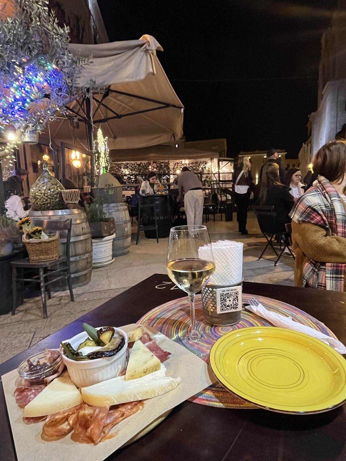 A cheese and charcuterie board with a glass of white wine at an outdoor table