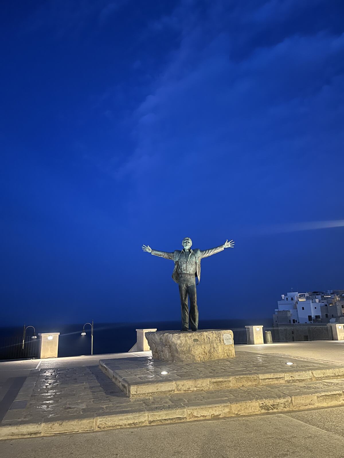 A statue with arms outstretched against a blue dusk sky in Polignano